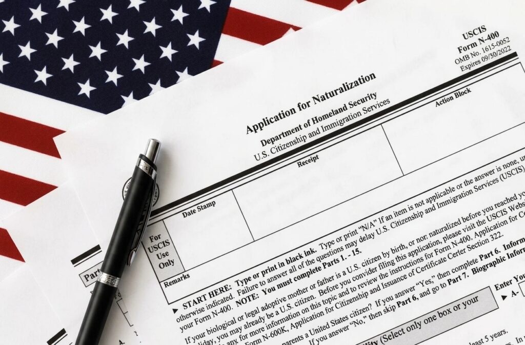 Official USCIS N-400 form 'Application for Naturalization' with a black pen and an American flag background, representing the U.S. citizenship application process.